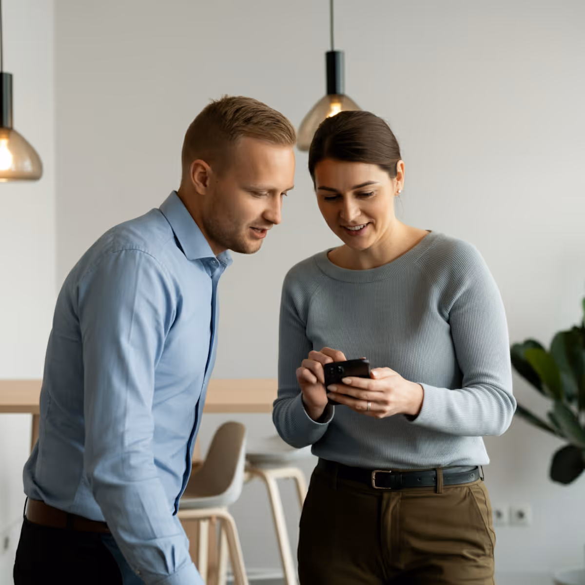 Dois colegas de trabalho em um escritório olhando juntos para um celular com interesse.