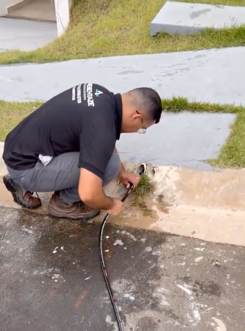 Homem agachado reparando um cabo de fibra óptica próximo a uma sarjeta em uma calçada.